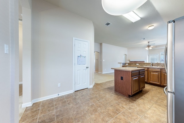 kitchen featuring stainless steel fridge, ceiling fan, sink, a kitchen island, and light tile patterned flooring