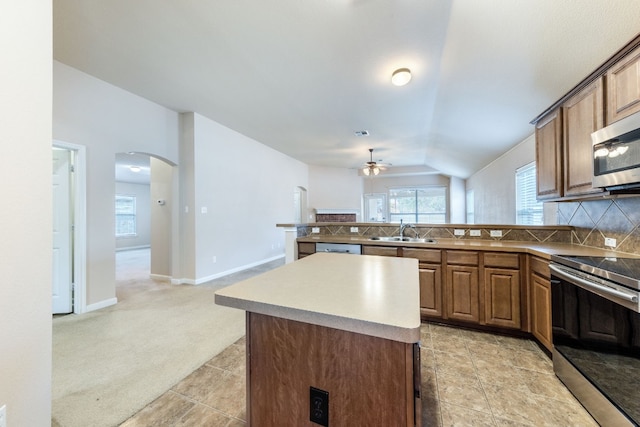 kitchen with lofted ceiling, sink, appliances with stainless steel finishes, tasteful backsplash, and a kitchen island