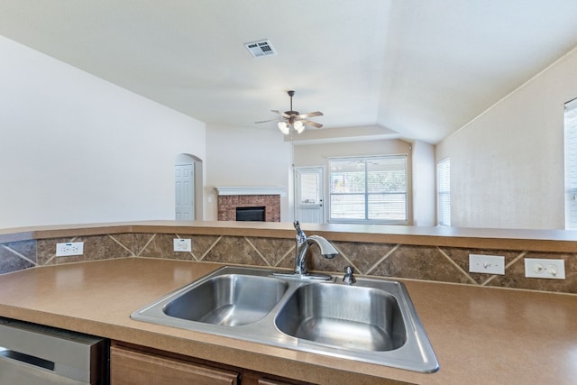 kitchen with ceiling fan, dishwasher, sink, a brick fireplace, and lofted ceiling