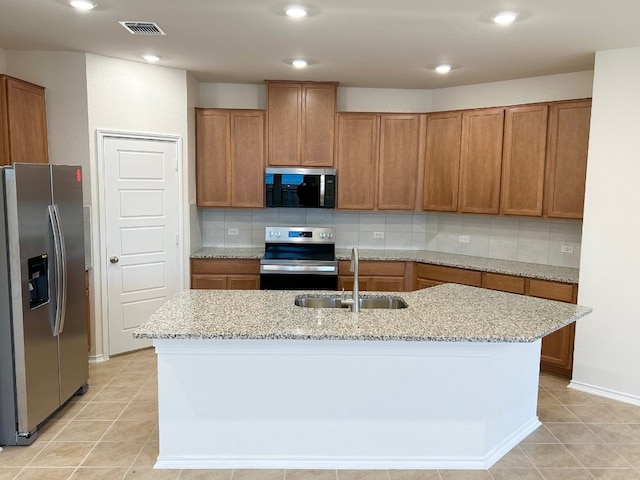 kitchen featuring decorative backsplash, light stone counters, stainless steel appliances, sink, and a center island with sink