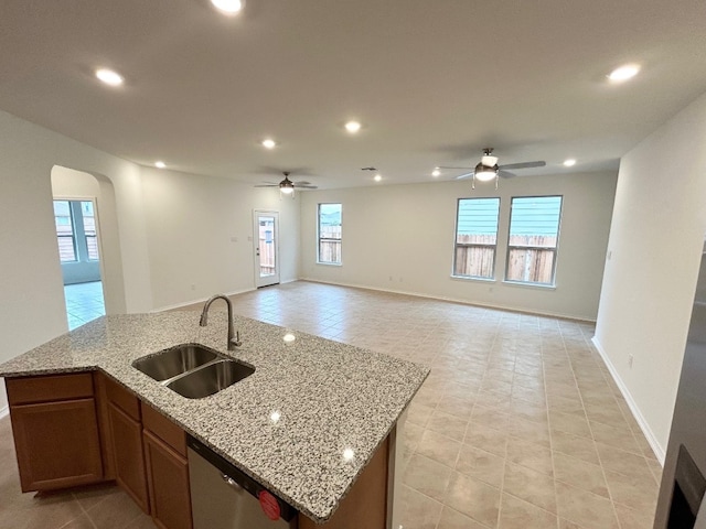 kitchen with ceiling fan, sink, light stone counters, stainless steel dishwasher, and an island with sink