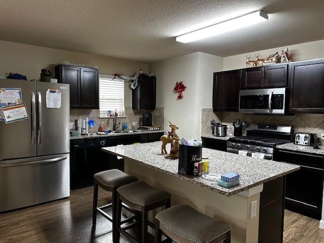 kitchen with appliances with stainless steel finishes, a kitchen island, a kitchen breakfast bar, and wood-type flooring