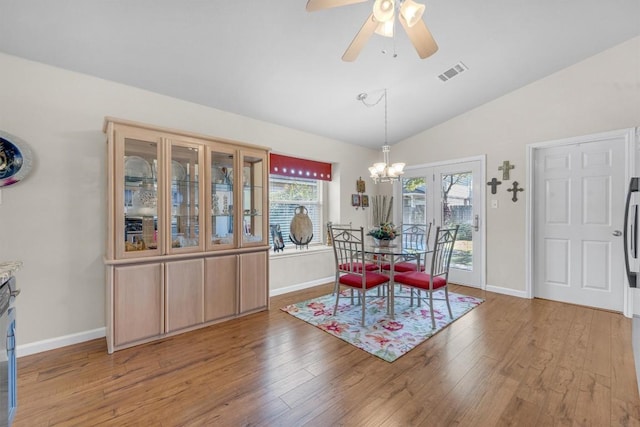 dining space with ceiling fan with notable chandelier, lofted ceiling, and light wood-type flooring