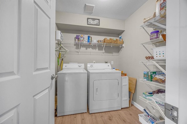 clothes washing area featuring independent washer and dryer, light wood-type flooring, and a textured ceiling