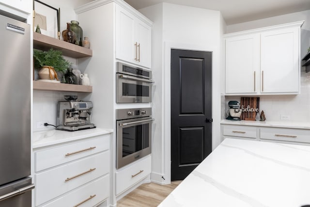 kitchen with white cabinets, stainless steel appliances, light wood-type flooring, and light stone countertops