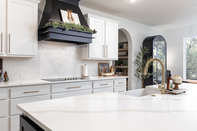 kitchen with tasteful backsplash, black electric stovetop, premium range hood, white cabinets, and sink