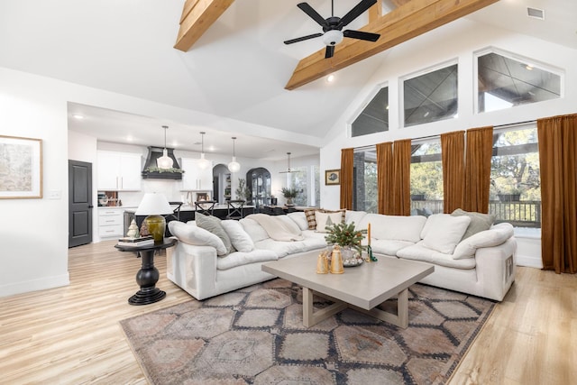 living room with high vaulted ceiling, ceiling fan, light hardwood / wood-style floors, and beam ceiling