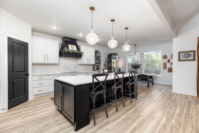 kitchen with pendant lighting, a center island with sink, custom range hood, black electric stovetop, and white cabinetry