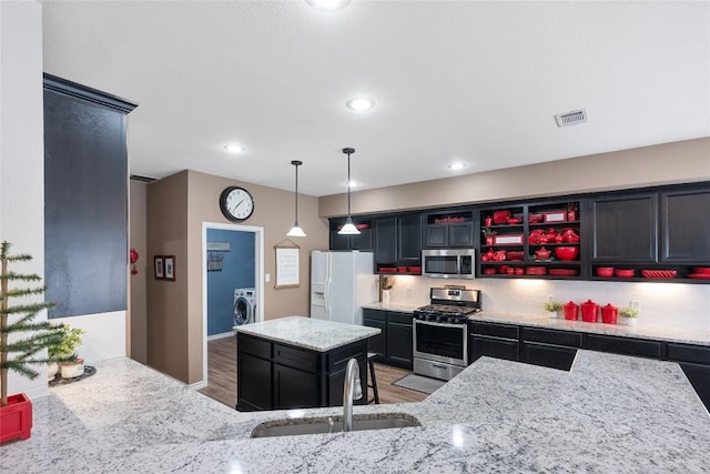 kitchen with sink, light wood-type flooring, appliances with stainless steel finishes, a kitchen island, and washer / clothes dryer