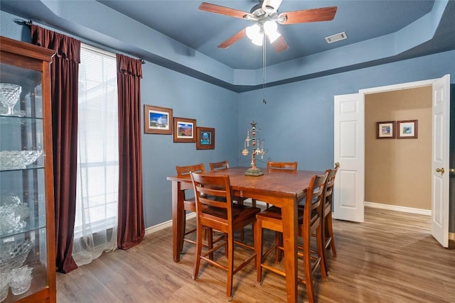 dining area with hardwood / wood-style flooring, ceiling fan, and a tray ceiling