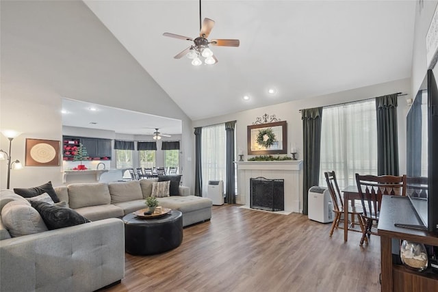 living room featuring a fireplace, wood-type flooring, high vaulted ceiling, and ceiling fan