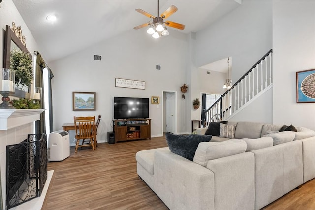 living room featuring ceiling fan, light hardwood / wood-style floors, a fireplace, and high vaulted ceiling