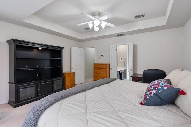 bedroom with a raised ceiling, ensuite bath, ceiling fan, and light colored carpet