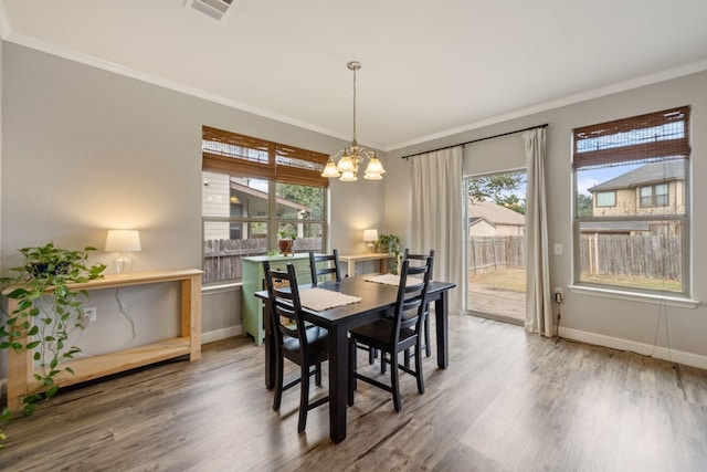 dining area with hardwood / wood-style floors, crown molding, a healthy amount of sunlight, and a notable chandelier