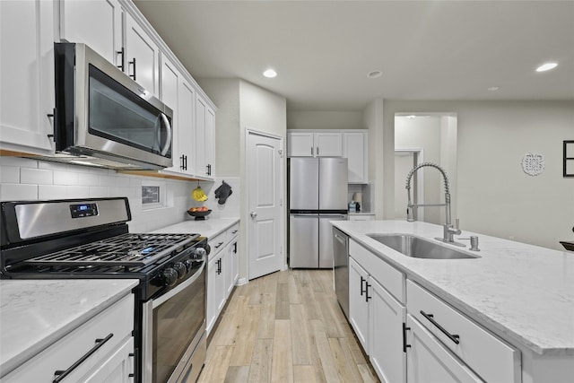 kitchen featuring a kitchen island with sink, white cabinets, sink, light hardwood / wood-style flooring, and appliances with stainless steel finishes