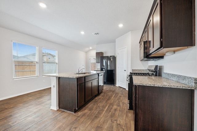 kitchen featuring black appliances, a center island with sink, sink, dark hardwood / wood-style flooring, and light stone counters