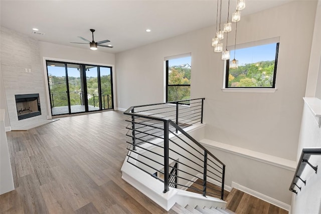 stairway with hardwood / wood-style floors, ceiling fan with notable chandelier, plenty of natural light, and a tile fireplace