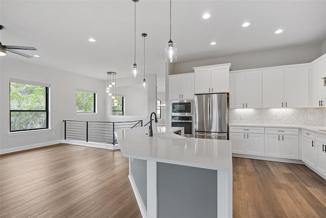 kitchen featuring stainless steel appliances, white cabinetry, pendant lighting, and a center island with sink