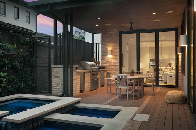 deck at dusk featuring a swimming pool with hot tub, a grill, and exterior kitchen