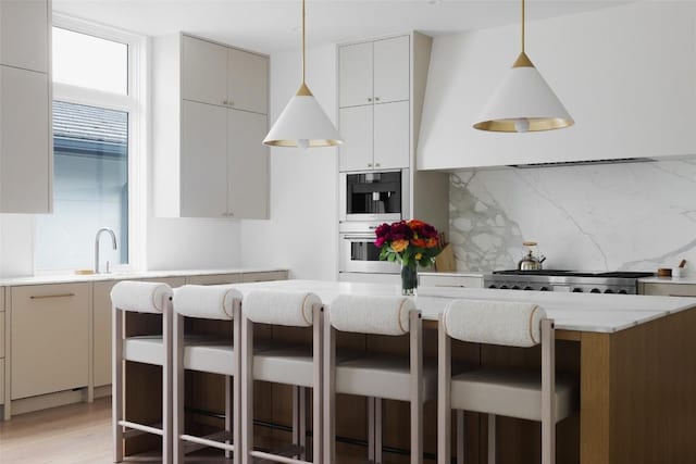 kitchen featuring stainless steel appliances, tasteful backsplash, light hardwood / wood-style floors, decorative light fixtures, and a breakfast bar