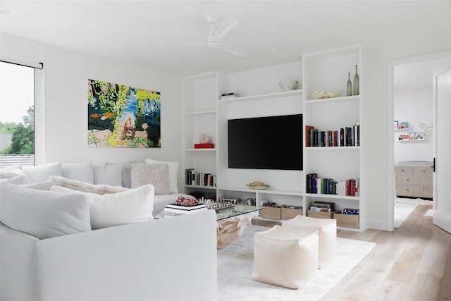 living room featuring light hardwood / wood-style floors, built in features, and ceiling fan