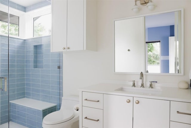 bathroom with tiled shower, vanity, toilet, and plenty of natural light