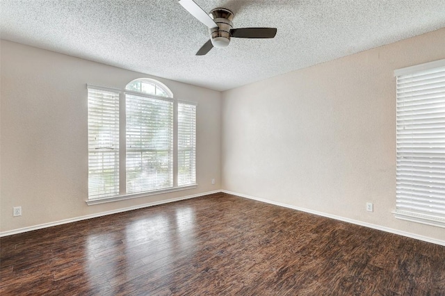 spare room with a textured ceiling, ceiling fan, dark wood-type flooring, and a wealth of natural light