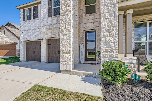 view of exterior entry featuring stone siding, brick siding, an attached garage, and driveway