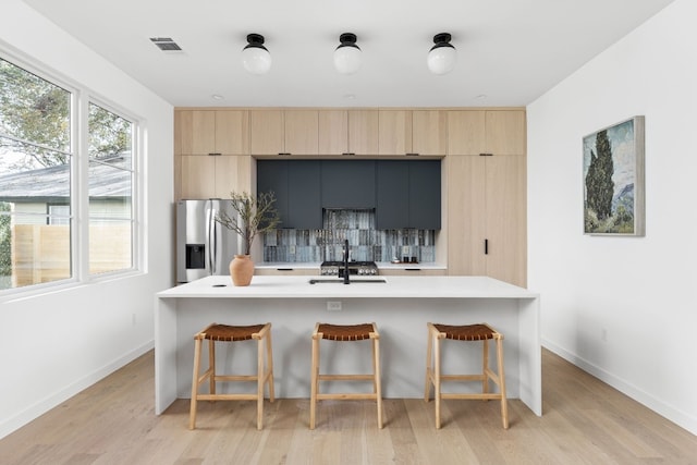 kitchen with sink, stainless steel refrigerator with ice dispenser, light hardwood / wood-style floors, a breakfast bar area, and a center island with sink