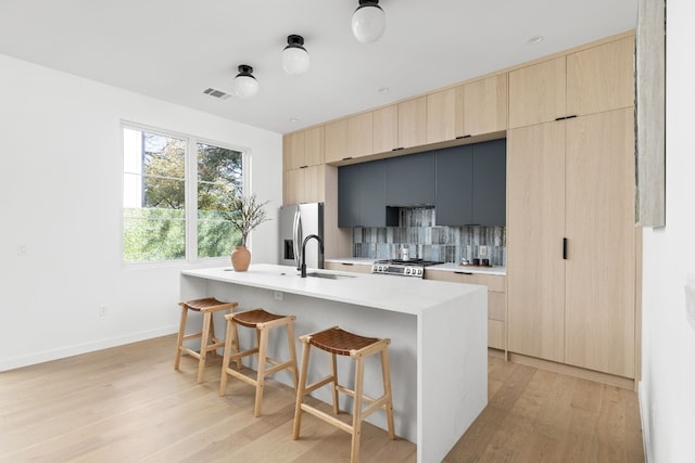 kitchen with a center island with sink, light hardwood / wood-style flooring, appliances with stainless steel finishes, tasteful backsplash, and a kitchen bar