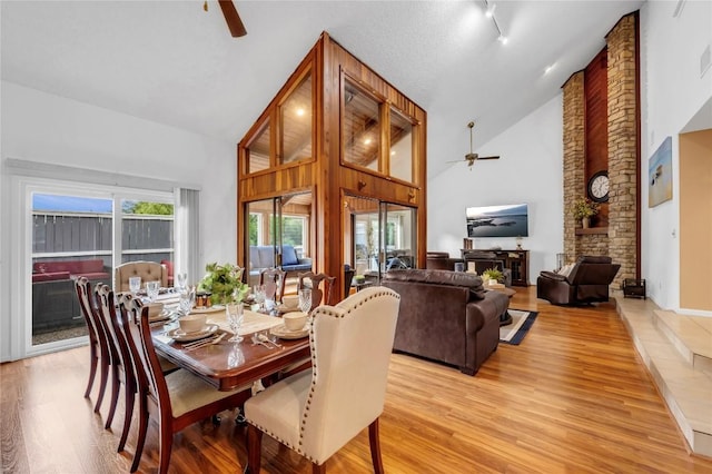 dining room with ceiling fan, high vaulted ceiling, and light hardwood / wood-style flooring