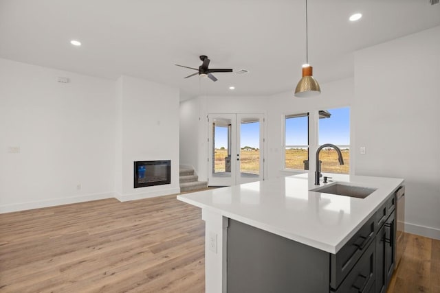 kitchen with a kitchen island with sink, french doors, sink, hanging light fixtures, and light hardwood / wood-style flooring