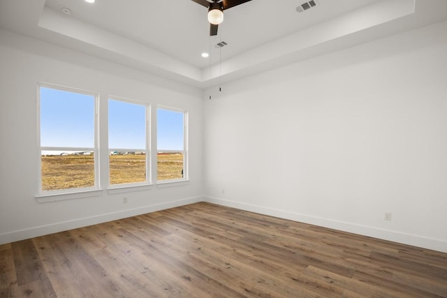 empty room with a tray ceiling, ceiling fan, and hardwood / wood-style floors