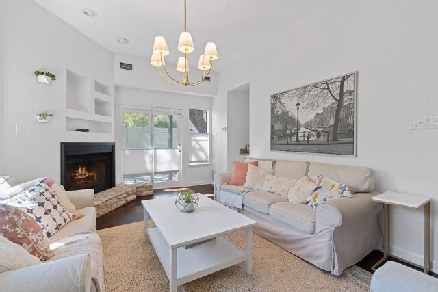 living room featuring a fireplace, light hardwood / wood-style flooring, built in shelves, and a notable chandelier