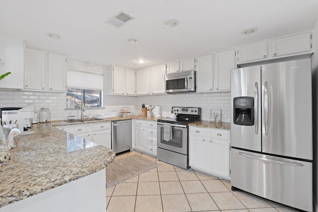 kitchen with light stone countertops, stainless steel appliances, sink, light tile patterned floors, and white cabinets