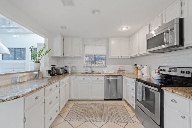 kitchen featuring a skylight, stainless steel appliances, white cabinets, decorative backsplash, and light tile patterned flooring