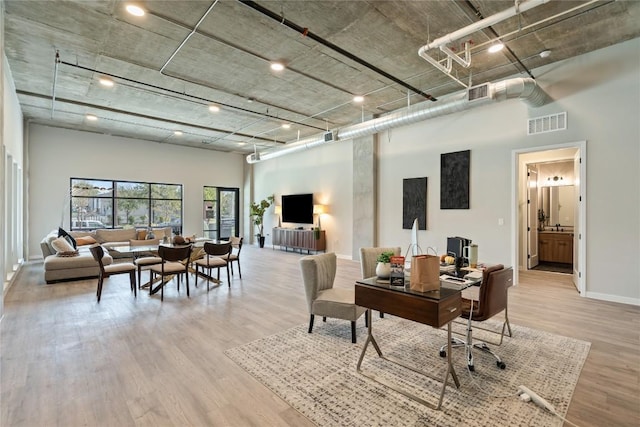 office area featuring light wood-type flooring and a towering ceiling