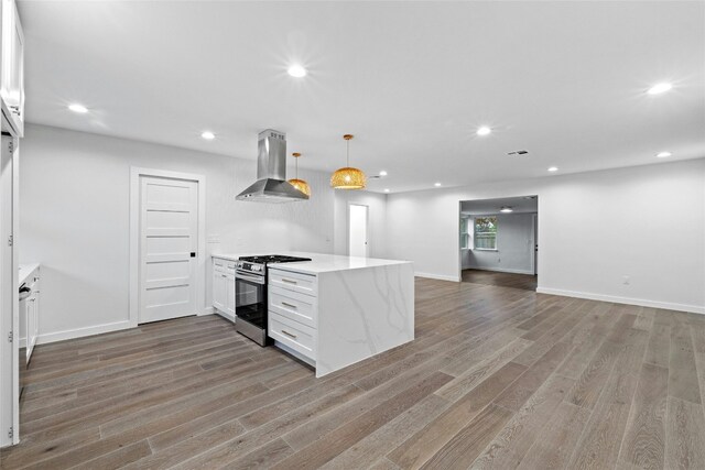 kitchen with stainless steel gas range oven, island range hood, decorative light fixtures, hardwood / wood-style flooring, and white cabinets