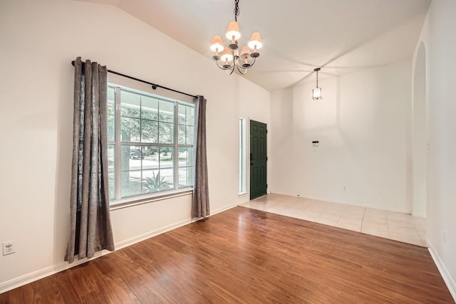 spare room featuring wood-type flooring, vaulted ceiling, and a notable chandelier