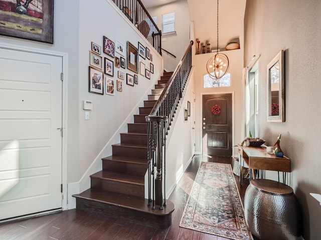 foyer entrance featuring a towering ceiling, dark hardwood / wood-style flooring, and an inviting chandelier