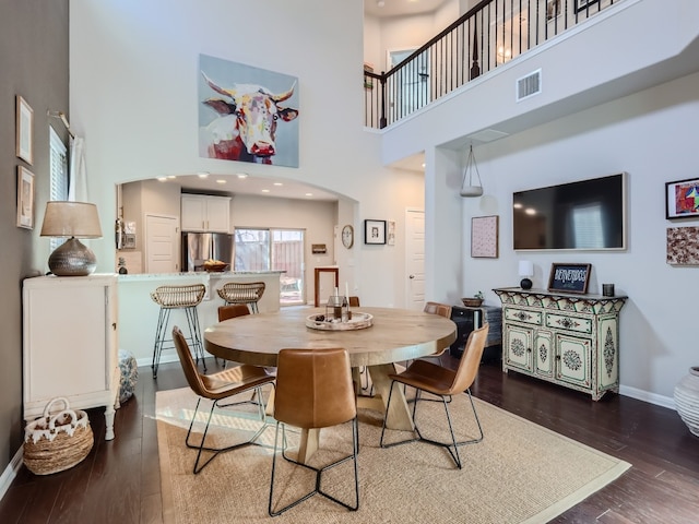 dining room featuring a towering ceiling and dark wood-type flooring