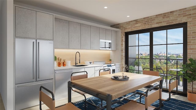 kitchen with sink, light hardwood / wood-style flooring, brick wall, and appliances with stainless steel finishes