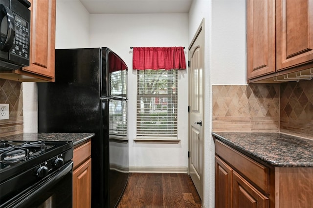 kitchen with black appliances, dark hardwood / wood-style floors, dark stone countertops, and backsplash