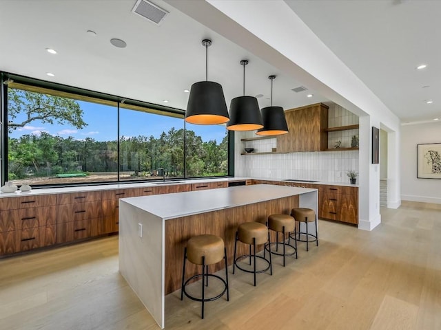 kitchen featuring decorative light fixtures, backsplash, light hardwood / wood-style floors, and a breakfast bar area