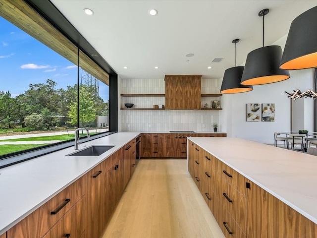 kitchen featuring light wood-type flooring, tasteful backsplash, hanging light fixtures, and sink