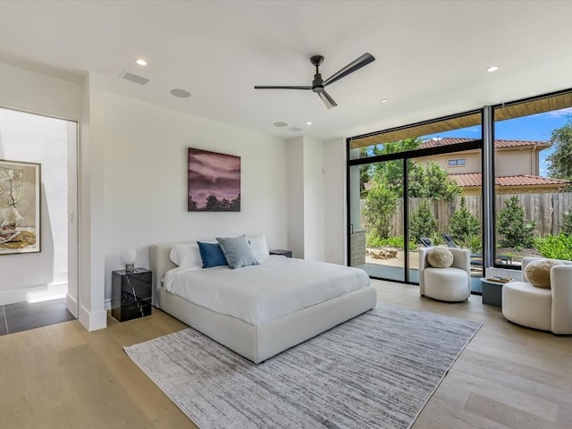 bedroom featuring ceiling fan, access to exterior, a wall of windows, and light hardwood / wood-style flooring