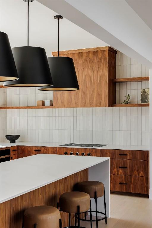 kitchen featuring a kitchen bar, tasteful backsplash, stovetop, and range hood