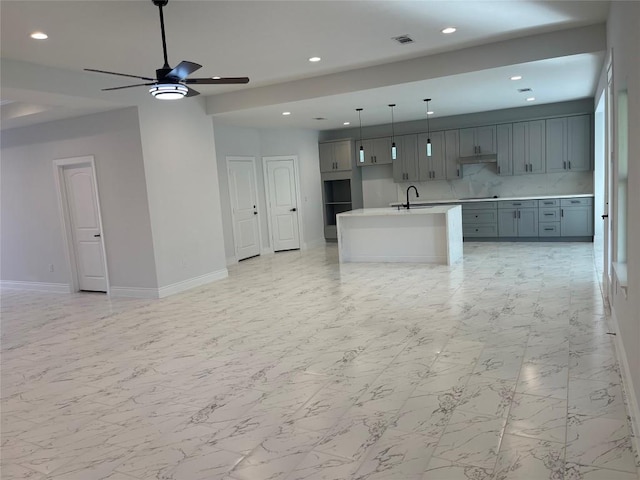 kitchen with backsplash, gray cabinetry, a kitchen island with sink, sink, and decorative light fixtures