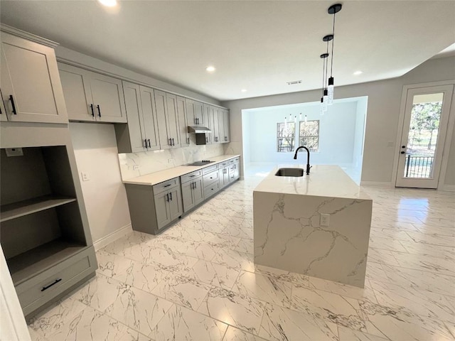 kitchen with light stone countertops, a kitchen island with sink, sink, gray cabinets, and hanging light fixtures