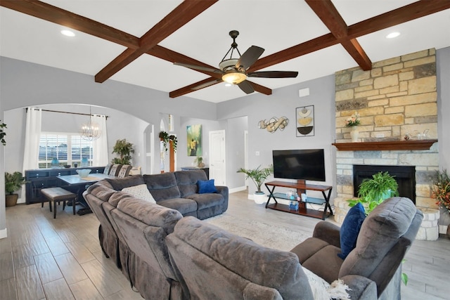 living room featuring a fireplace, light hardwood / wood-style flooring, beamed ceiling, and ceiling fan with notable chandelier